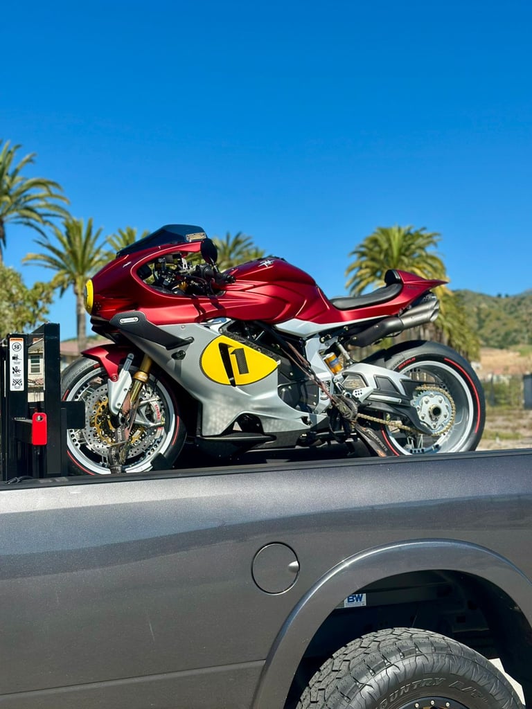 Red and white sport motorcycle with yellow accents parked in sunny desert setting with palm trees and mountains in background